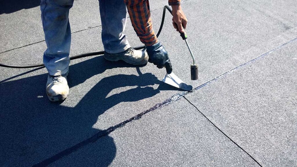 Homeowner inspecting roof shingles from a ladder beside a house with clean gutters and nearby trees
