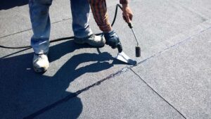 Homeowner inspecting roof shingles from a ladder beside a house with clean gutters and nearby trees