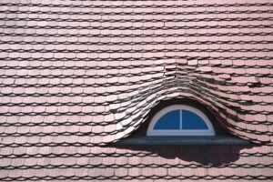 Inspector examining roof shingles and flashing beside a residential attic access hatch.