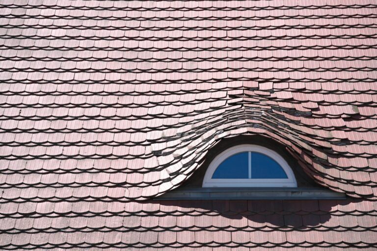 Inspector examining roof shingles and flashing beside a residential attic access hatch.